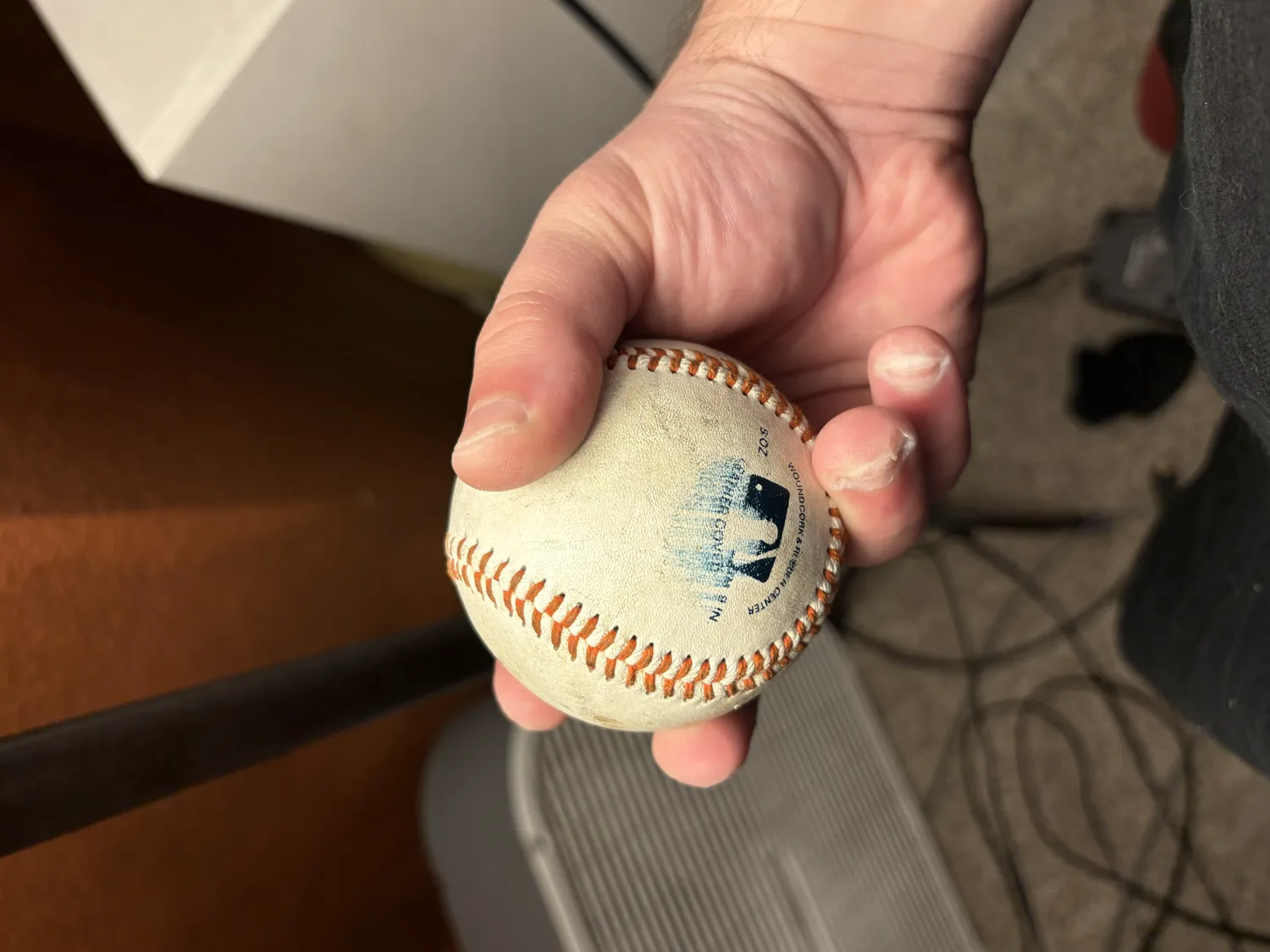 A right hand gripping a baseball four-seam style, two fingertips crossing the horseshoe seam with the thumb underneath.