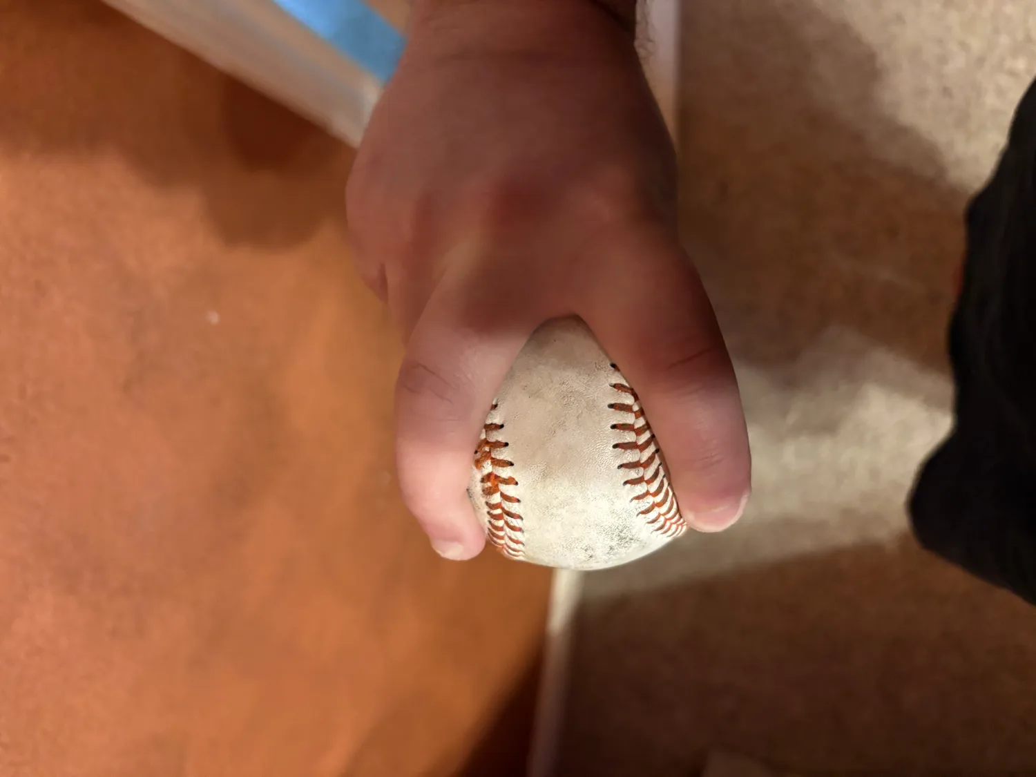 A hand gripping a baseball split-finger style, index and middle fingers spread wide just outside the seams.